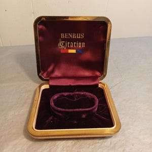 May include: Open vintage watch box with a gold-colored frame and a burgundy velvet interior. The box is labeled "BENRUS Citation" in gold lettering. The interior features a velvet cushion to hold a watch or bracelet.