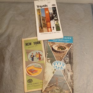 May include: Three vintage travel guides from the Automobile Club of New York. The guides include a "Triptik" with scenic images, a "New York Vertical File" with illustrations, and a New York City street map. The guides feature the AAA logo.