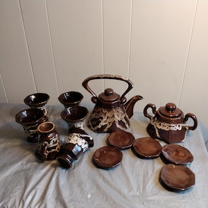 May include: A brown and white ceramic tea set with a teapot, creamer, six cups, and six saucers. The set has a unique speckled glaze.