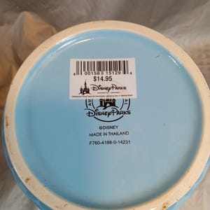 Pu&ograve; includere: Base di una tazza Disney Parks in ceramica azzurra con bordo bianco. Il fondo della tazza presenta il logo Disney Parks, la scritta "&copy;DISNEY MADE IN THAILAND" e un codice a barre.