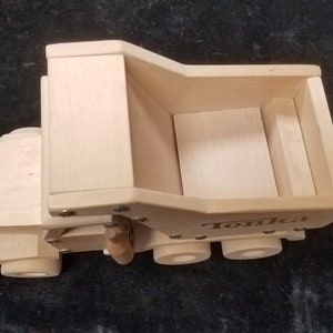 Könnte beinhalten: Ein hölzerner Spielzeug-Kipplaster mit dem Wort "Tonka" auf der Seite. Der Laster ist hellbraun und hat eine hochgeklappte Ladefläche.
