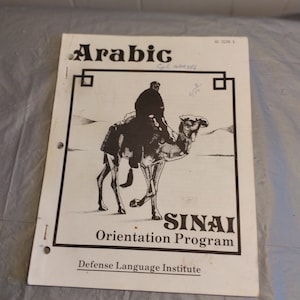 May include: A black and white illustration of a person riding a camel in the desert. The text "Arabic Sinai Orientation Program Defense Language Institute" is printed below the image.