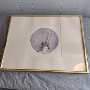 May include: A framed black and white print of a person wearing a tall hat and looking to the side. The print is in a circular frame and has a purple background.
