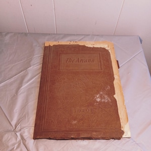 Puede incluir: Un libro encuadernado en cuero marrón con el título "The Arcana" y el año "1929" en relieve en la portada.