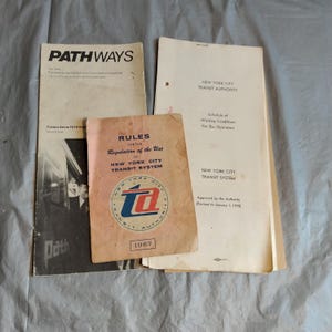 以下が含まれることがあります： ニューヨーク市交通局のヴィンテージ文書3点。 上部の文書は「PATHWAYS」というタイトルの雑誌。 中央の文書は「RULES FOR THE REGULATION OF THE USE OF NEW YORK CITY TRANSIT SYSTEM」というテキストと1967年が記載されたニューヨーク市交通システムの規則書。 下部の文書はバス運転手の労働条件のスケジュールです。