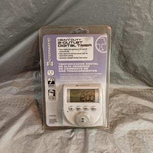 May include: An Intermatic heavy duty 2-outlet digital timer in its original clear plastic packaging. The white device features a digital display showing 12:00, four circular control buttons labelled OK, MODE, PROG, ON/OFF, and a central dial.