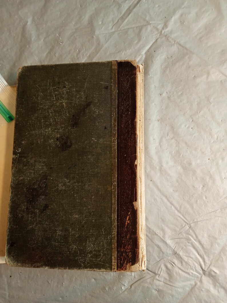 May include: An antique book with a worn, dark green cover and a brown spine. The cover shows signs of age with visible wear and tear. The spine is a darker brown, and the pages have a yellowed appearance, suggesting the book's age.
