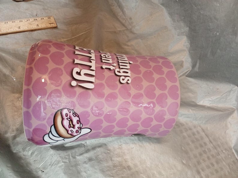 Puede incluir: Un vaso rosa con un patr&oacute;n de corazones y las palabras "pretty things" en blanco. Tambi&eacute;n se muestra un dibujo animado de una rosquilla con glaseado rosa y chispas.