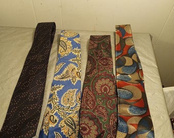 May include: Four neckties with various patterns are displayed. One is navy with small dots, another is blue with a paisley design, a third is burgundy with a floral pattern, and the last is red, blue, and tan with an abstract design.