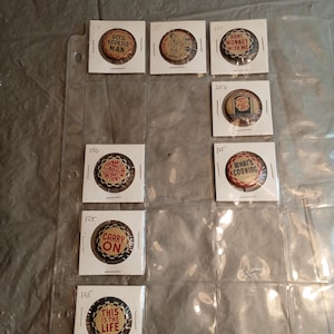 May include: A collection of vintage pinback buttons displayed in a clear plastic sheet. The buttons feature various phrases and designs, including "SO'S YOUR OLD MAN" and "CARRY ON". The buttons are in a variety of colors, including red, white, and brown.