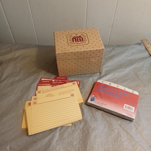 May include: A tan recipe box with a red and brown floral pattern and a matching lid. Several recipe cards and a set of A-Z recipe dividers are next to the box. The recipe cards are yellow with red accents.