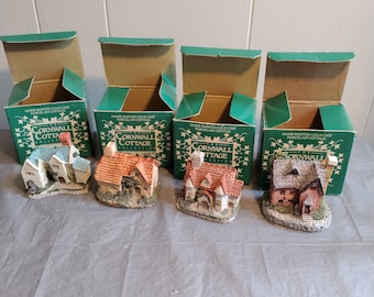 Może przedstawiać: Cztery zielone pudełka z ręcznie malowanymi, zimnoodlewanymi domkami z porcelany. Każde pudełko ma napis "The Cornwall Cottage Collection" na przodzie.
