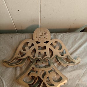Puede incluir: Objeto decorativo de metal en forma de ángel con intrincados diseños calados. El ángel tiene alas extendidas y una cara estilizada. El metal tiene un aspecto brillante, dorado. Adecuado para la decoración del hogar.