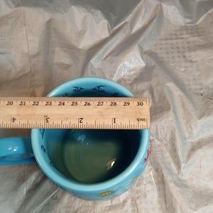 May include: A light blue ceramic mug with a handle, featuring a sea life design. The mug has a diameter of approximately 4 inches. The interior is green, and the rim is decorated with fish illustrations.