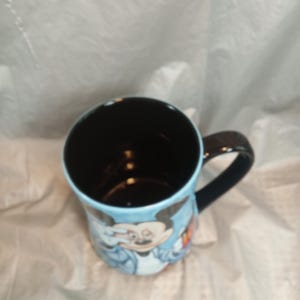 Pu&ograve; includere: Una tazza in ceramica con il personaggio dei cartoni animati Mickey Mouse. La tazza ha un interno e un manico neri, con un esterno azzurro. Mickey Mouse &egrave; raffigurato con una giacca blu. La tazza &egrave; di dimensioni standard per bevande calde.