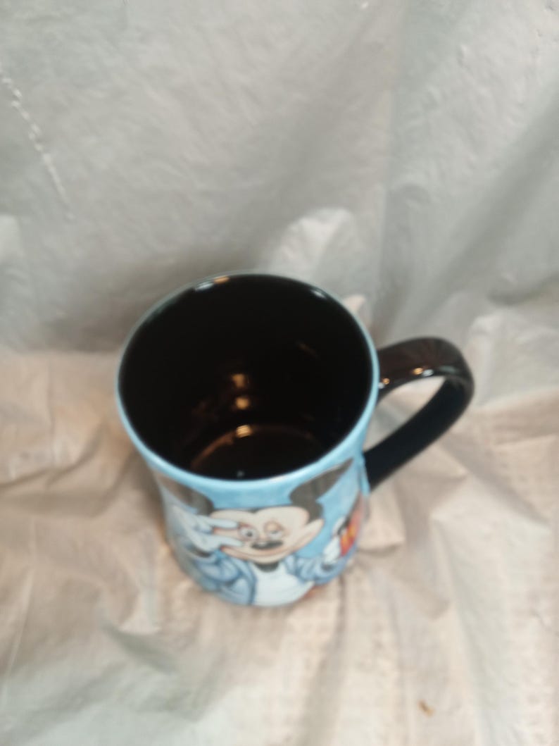 Pu&ograve; includere: Una tazza in ceramica con il personaggio dei cartoni animati Mickey Mouse. La tazza ha un interno e un manico neri, con un esterno azzurro. Mickey Mouse &egrave; raffigurato con una giacca blu. La tazza &egrave; di dimensioni standard per bevande calde.