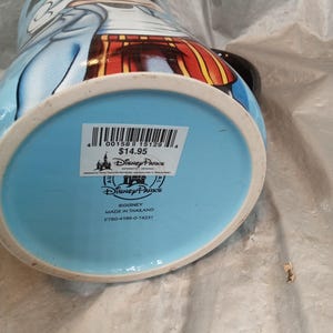 Pu&ograve; includere: Una tazza in ceramica Disney Parks con Topolino in un completo blu e rosso. La tazza ha un manico nero e una base azzurra. Il fondo della tazza presenta un logo e un testo Disney Parks.