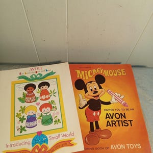 May include: Two vintage Avon books. One is a coloring book featuring Mickey Mouse, with the text "Invites you to be an Avon Artist." The other book is titled "Small World" and features illustrations of dolls.