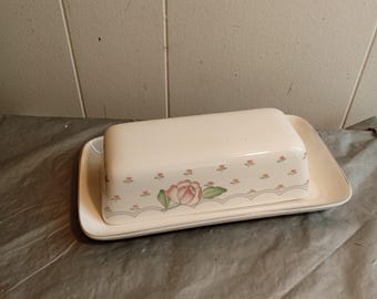 Könnte beinhalten: Eine weiße Keramik-Butterdose mit Deckel, die auf einem passenden rechteckigen Tablett steht. Der Deckel hat ein Blumenmuster mit rosa und grünen Akzenten. Die Dose ist zum Aufbewahren und Servieren von Butter bestimmt.