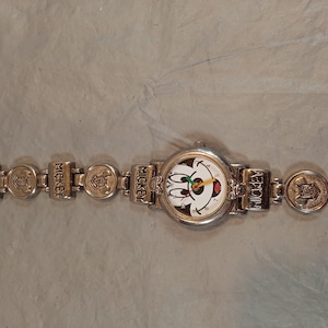 May include: A silver-toned analog wristwatch featuring a round face with a Mickey Mouse graphic. The watch band consists of alternating rectangular links embossed with the word MICKEY and circular links featuring a raised character emblem.