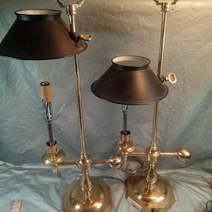 May include: Two brass lamps with octagonal bases, adjustable vertical stems, and black conical shades. Each lamp features a top handle, a side adjustment key, and a central socket. A ruler is visible in the lower left corner for scale reference.
