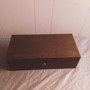May include: A dark brown wooden box with a lock and keyhole on the front. The box is sitting on a white surface.