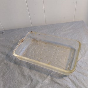 May include: A clear glass baking dish with a raised grid pattern on the bottom. The dish has a slightly yellowed tint and shows signs of wear.