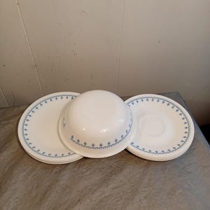 May include: A set of white ceramic dishes with a blue floral pattern. The set includes plates and a bowl. The plates and bowl are arranged on a gray surface. The dishes are clean and appear to be in good condition.