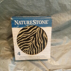 May include: A NatureStone box containing four absorbent coasters with a black and tan zebra stripe pattern. The packaging features the brand name NatureStone in white text on a blue background, the number 4, and the text Absorbent Coasters and Coaster Holder.