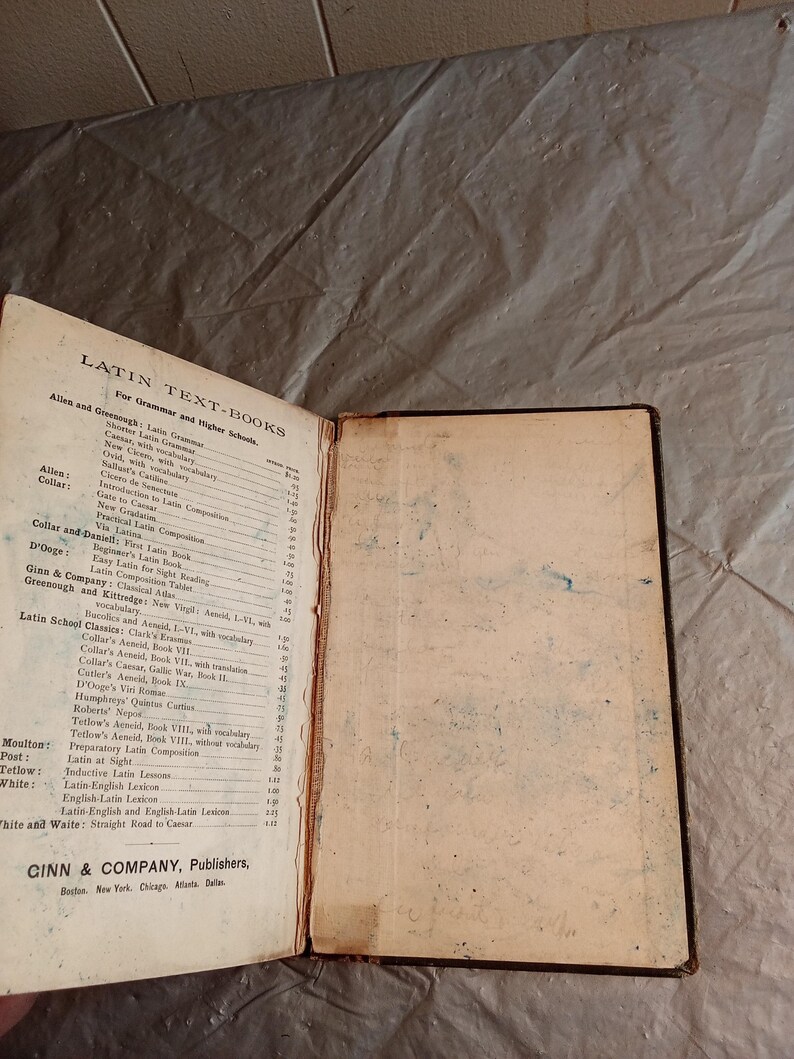 May include: An open vintage Latin textbook with a worn cover and pages. The left page displays a detailed table of contents for grammar and higher schools. The book is published by Ginn & Company.