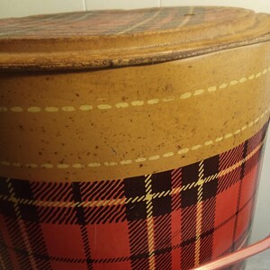 May include: Vintage metal bucket with a lid. The bucket features a red and black plaid pattern on the lower portion and a tan upper section with a dotted line design. The lid also has a plaid pattern. A pink handle is visible.