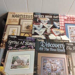 Pode incluir: Uma cole&ccedil;&atilde;o de oito livros de padr&otilde;es de ponto cruz com capas coloridas. Os t&iacute;tulos incluem "Narcissus Old Print Collection Book 1", "Kathie's Bread Cloths by Kathie R", "Spring At Stoneg Book 3", "Discovery of the New World" e "Apple Sampler".