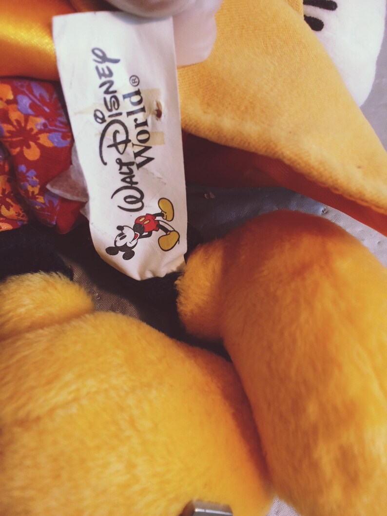 Puede incluir: Primer plano de un peluche con pelaje amarillo y una etiqueta blanca. La etiqueta dice "Walt Disney World" con un gr&aacute;fico de Mickey Mouse. El juguete tiene un aspecto suave y texturizado.