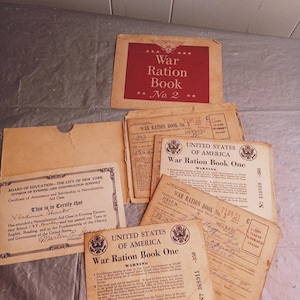 Può includere: Una collezione di documenti d'epoca della Seconda Guerra Mondiale, tra cui i War Ration Books e un Certificato di Frequenza. Il War Ration Book n. 2 è rosso con testo bianco. Gli altri documenti sono color cuoio con testo nero.