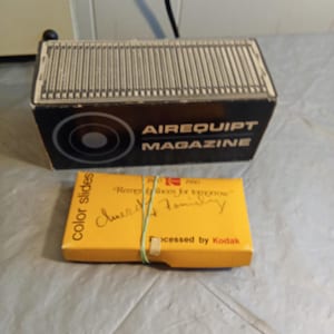 Könnte beinhalten: Eine schwarz-weiße "AIREQUIPT MAGAZINE" Box und eine gelbe Schachtel mit "color slides". Die gelbe Schachtel hat handschriftlichen Text und ein grünes Gummiband. Der Text "Processed by Kodak" ist sichtbar.