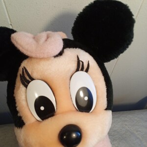 May include: A plush Minnie Mouse doll with a pink bow, black ears, and large, expressive eyes. The doll has a pink face and body, with a black nose and eyelashes. A classic Disney character.