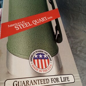May include: A green Stanley Aladdin steel quart bottle in its original packaging. The box features a red banner with the text America's #1 STEEL QUART Bottle, a circular logo with stars and stripes, and the text GUARANTEED FOR LIFE at the bottom.