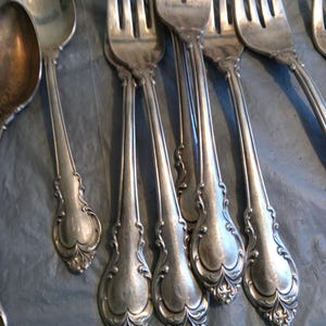 May include: A set of silver forks with ornate handles. The forks are arranged in a row, with the handles facing the viewer. The forks are all in good condition and have a shiny finish.