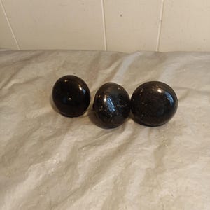Peut inclure: Trois objets sphériques sombres et brillants sont disposés en rangée. Les sphères ont un aspect poli, reflétant la lumière. L'arrière-plan est une surface claire et texturée.