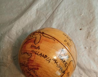 May include: A small, wooden globe with hand-drawn continents and text. The globe is light brown with darker brown markings and text, including "Nova Hollandia" and "Mare Pacificum".