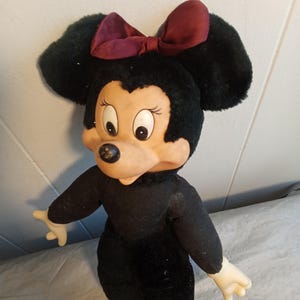 May include: A vintage Minnie Mouse plush doll. The doll has a black body, large black ears, and a burgundy bow. The face is tan with large eyes and a black nose. The doll is wearing burgundy shoes and has white hands.