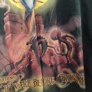 May include: Black t-shirt featuring a scene from "Tim Burton's The Nightmare Before Christmas." The design includes Jack Skellington, a dragon-like creature, and the text "Nightmare Before Christmas" in a stylized font, set against a moonlit background.