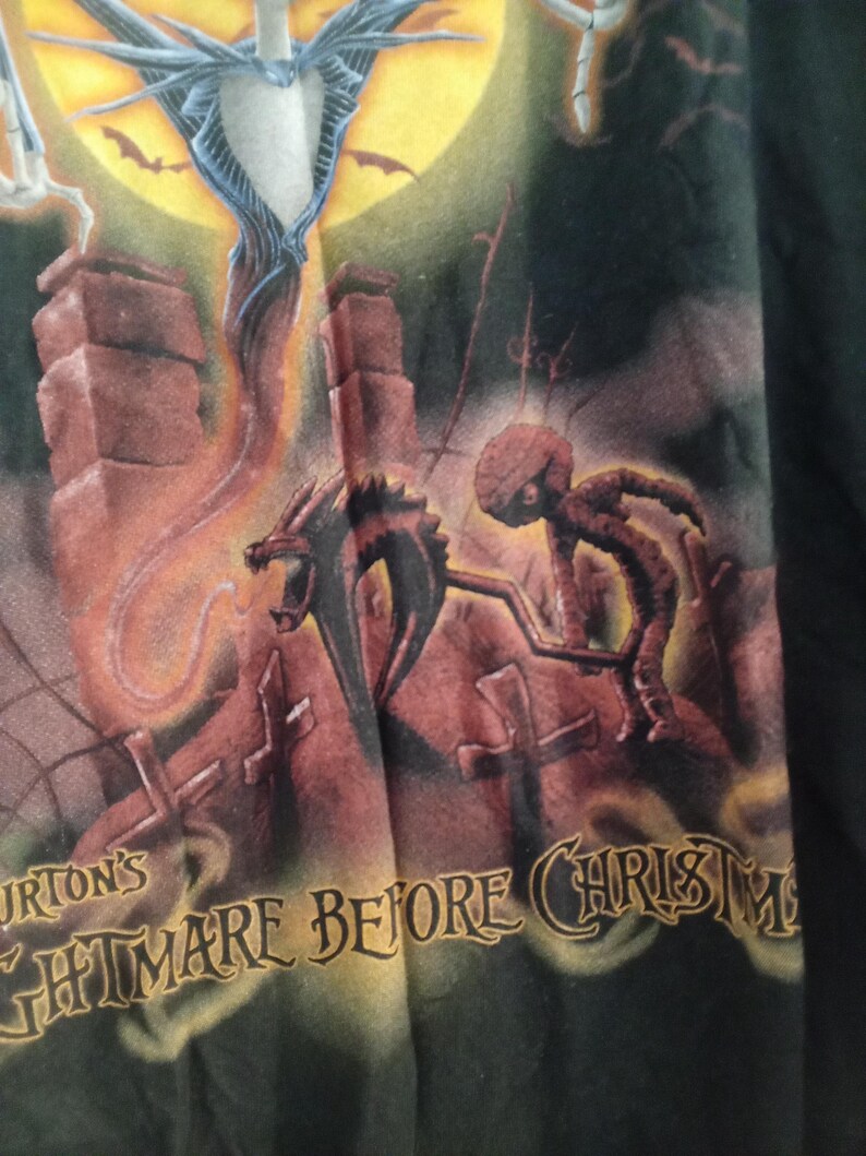 May include: Black t-shirt featuring a scene from "Tim Burton's The Nightmare Before Christmas." The design includes Jack Skellington, a dragon-like creature, and the text "Nightmare Before Christmas" in a stylized font, set against a moonlit background.