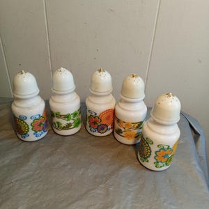 Puede incluir: Cinco saleros y pimenteros de cerámica blanca con diseños florales coloridos. Cada salero y pimentero tiene un cuerpo redondeado y una parte superior cónica. Los diseños florales incluyen naranja, amarillo, azul y verde.