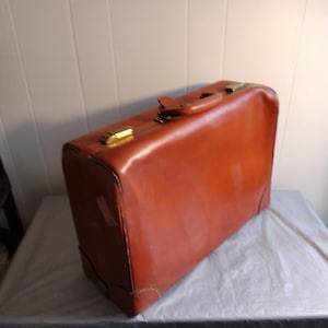 Könnte beinhalten: Ein vintage brauner Lederkoffer mit Messingbeschlägen. Der Koffer hat ein klassisches Design und ist in gutem Zustand.