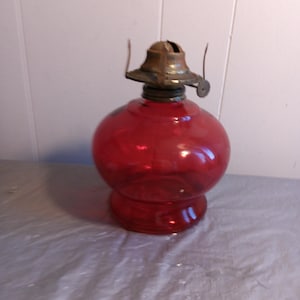 Op de afbeelding: Een rode glazen olielamp met een messing lont houder en een glazen schoorsteen.