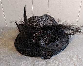 May include: A black straw hat with a black feather and a black ribbon. The hat has a wide brim and a tall crown.