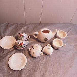 Puede incluir: Un juego de té de porcelana vintage con diseños florales. El juego incluye una tetera, una jarra de crema, un azucarero, cuatro tazas y cuatro platillos.