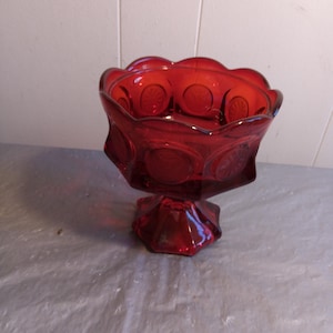 Puede incluir: Un plato de dulces de vidrio rojo con una base de pedestal. El plato tiene un borde festoneado y un patrón de pequeños círculos.