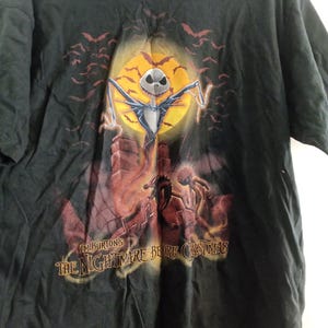 May include: Black t-shirt featuring a graphic from Tim Burton's "The Nightmare Before Christmas." The design includes Jack Skellington in front of a full moon, bats, and the film's title. The shirt is a short-sleeved crew neck.
